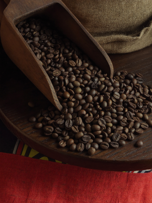 Dark roasted robusta coffee beans overflowing from a wooden scoop onto a burlap sack